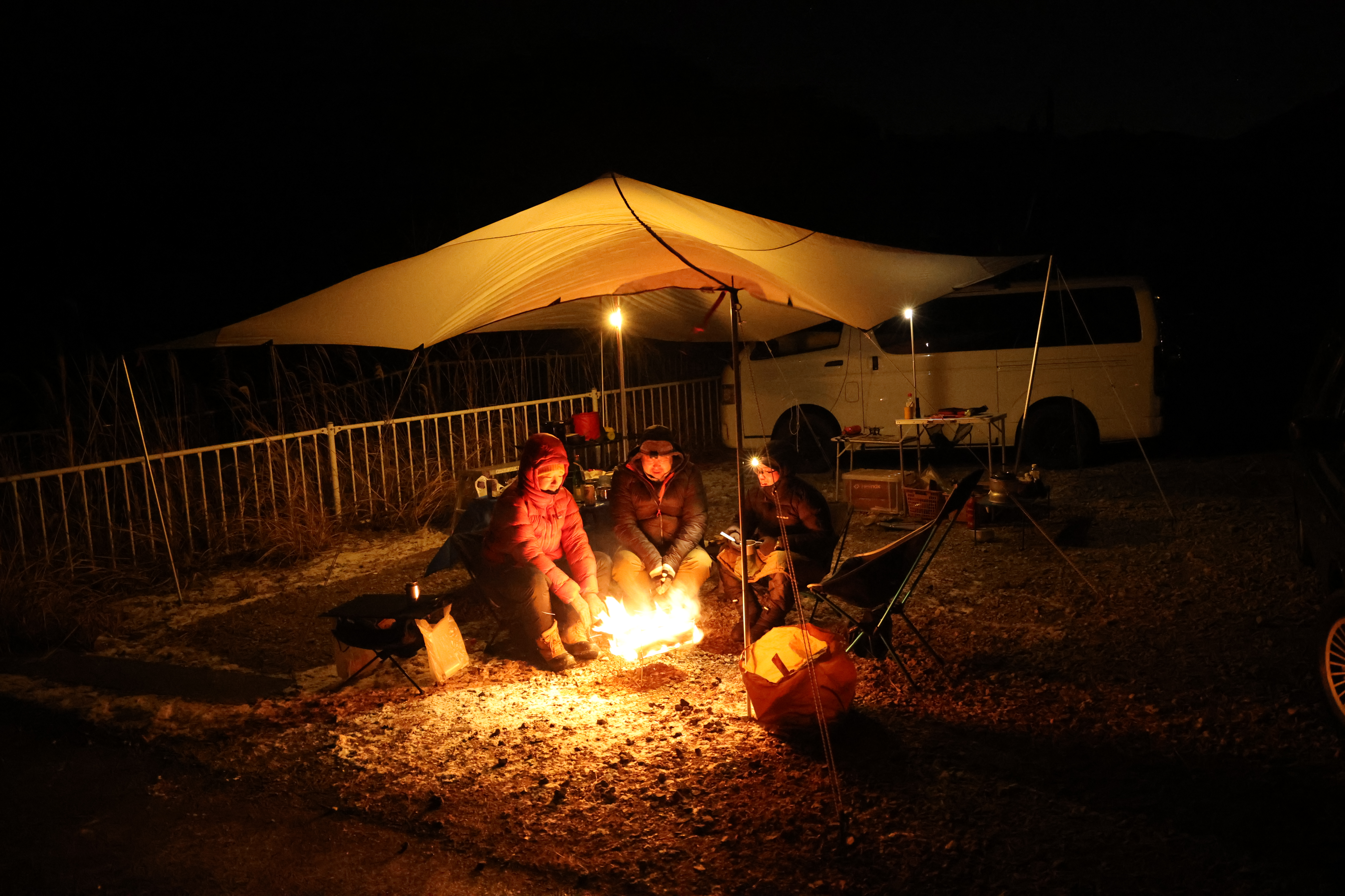ベースキャンプの夜。テンマクデザインの青空タープの下で焚火をかこんでくつろぐ参加者。